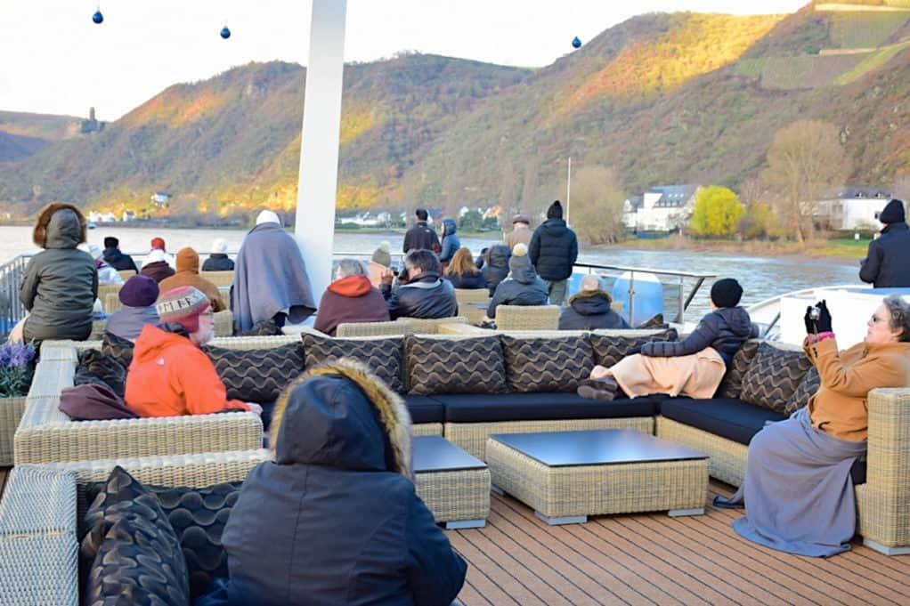 甲板上的乘客穿着外套和帽子沿着莱茵河。
